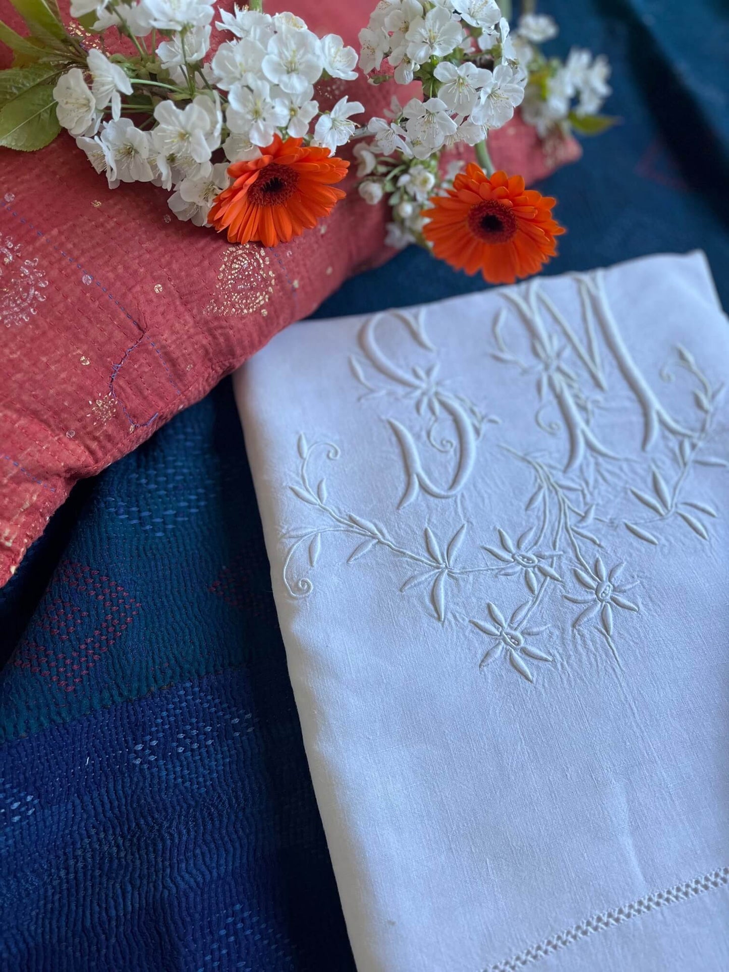 Drap ancien brodé monogramme SM, mis en scène avec kantha indigo et fleurs printanières – ambiance déco poétique