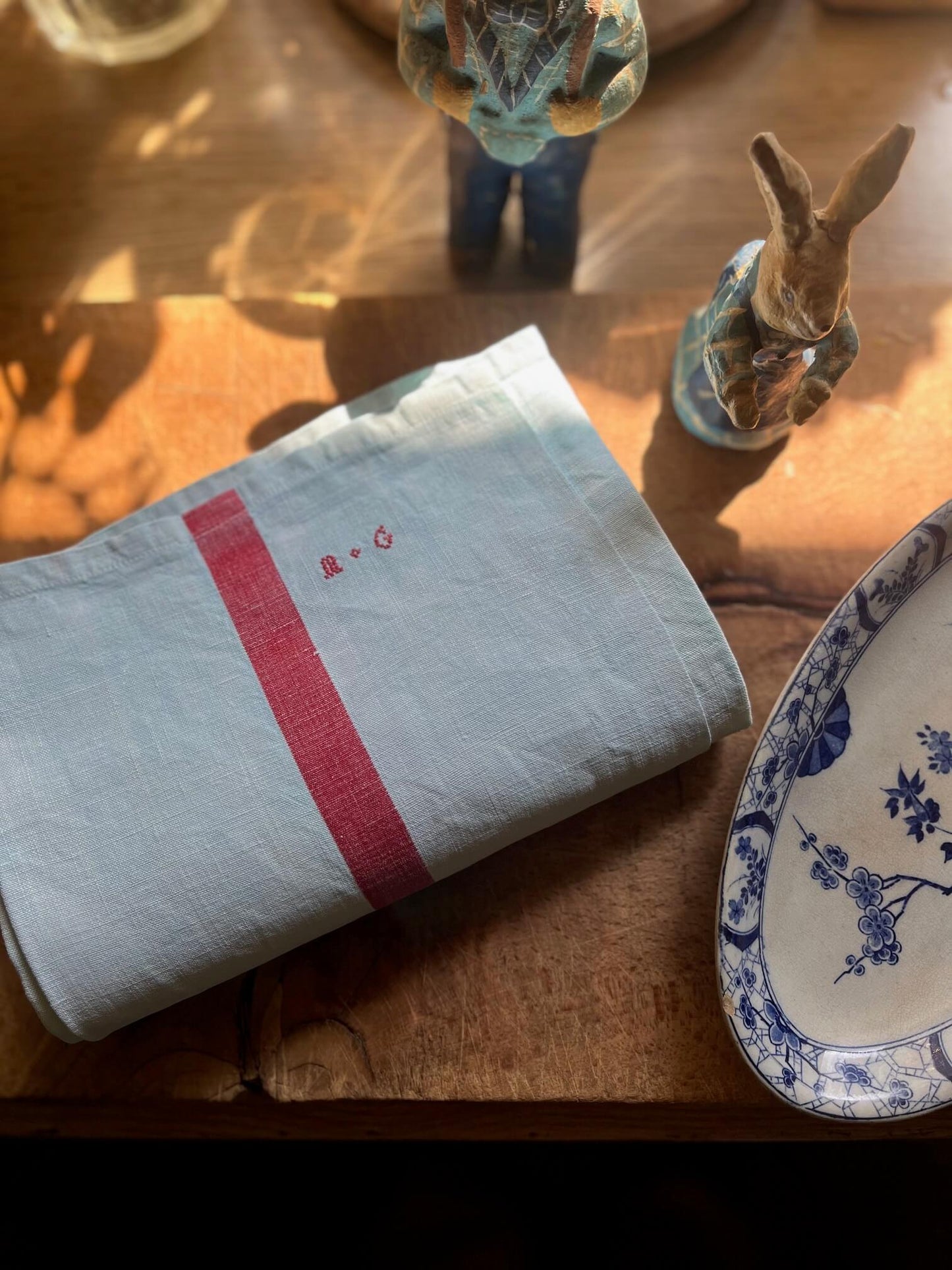 Torchon ancien en coton et lin teint vert d’eau, brodé et posé sur une table en bois.