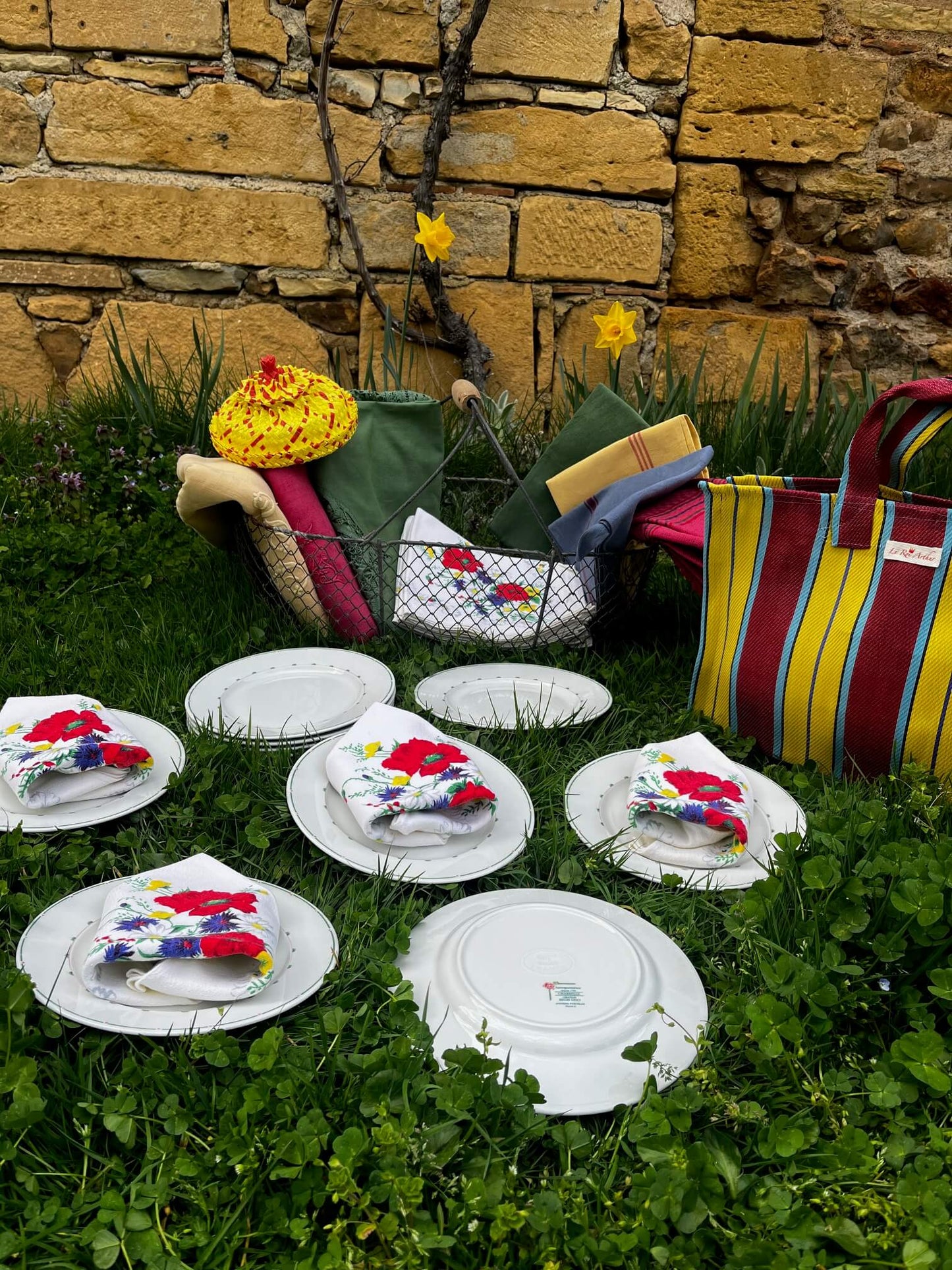 Table champêtre dressée sur l’herbe avec des serviettes vintage fleuries et de la vaisselle ancienne