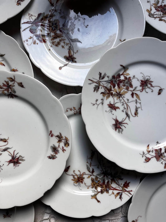 Assiettes anciennes en porcelaine blanche à décor floral bordeaux disposées sur nappe ancienne brodée