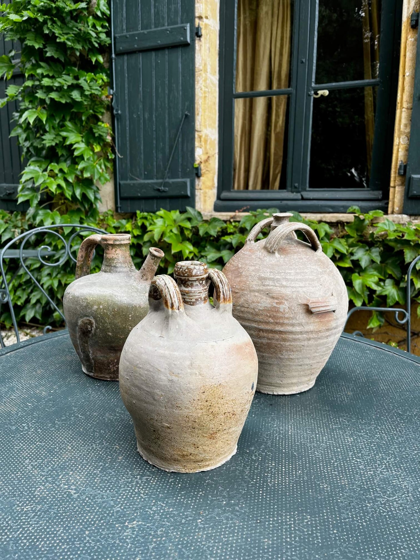 Accumulation de cruches anciennes utilisées en décoration dans un jardin ou salon rustique

