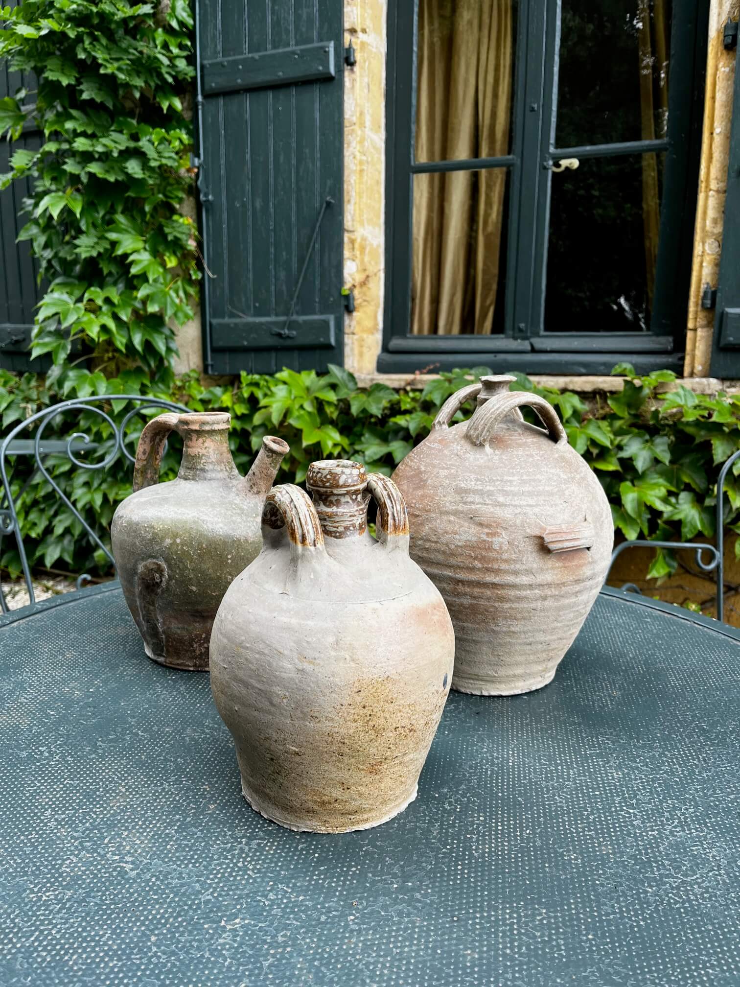 Accumulation de cruches anciennes utilisées en décoration dans un jardin ou salon rustique

