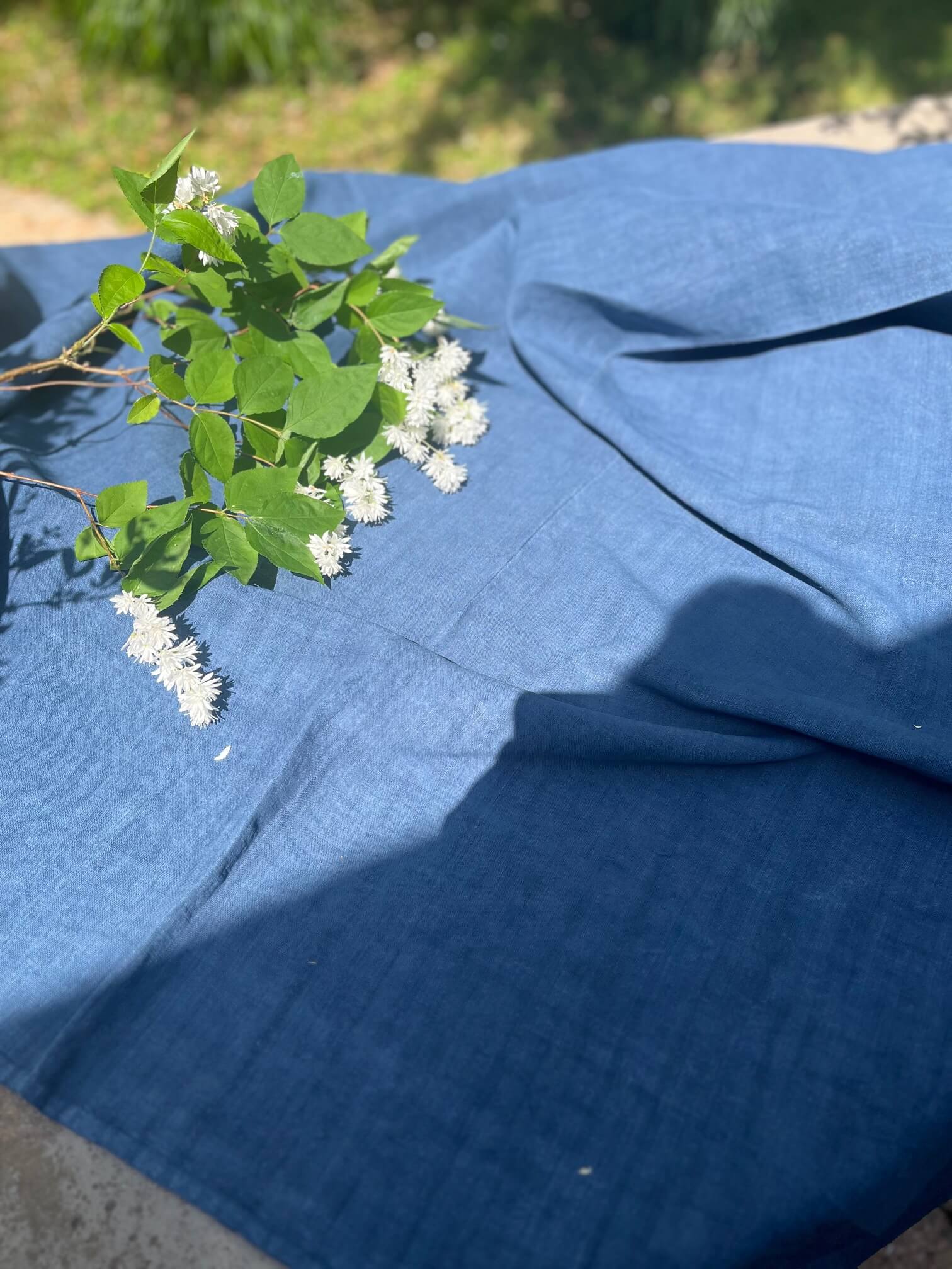 Nappe ancienne en linge ancien français teinte bleu nuit présentée en extérieur avec fleurs blanches